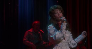 Movie still from “Coal Miner's Daughter” (1980), directed by Michael Apted – A woman singing into a microphone on a stage; Medium shot, Over the shoulder angle