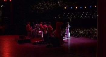 Movie still from “Coal Miner's Daughter” (1980), directed by Michael Apted – A woman in a white dress singing on a stage; Wide shot, Over the shoulder angle