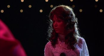 Movie still from “Coal Miner's Daughter” (1980), directed by Michael Apted – A woman in a white dress is standing in front of a microphone; Medium shot, Over the shoulder angle