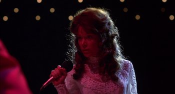 Movie still from “Coal Miner's Daughter” (1980), directed by Michael Apted – A woman in a white dress is holding a microphone; Close Up shot, Low angle