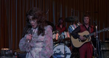Movie still from “Coal Miner's Daughter” (1980), directed by Michael Apted – A woman singing into a microphone in front of a band; Medium shot, Over the shoulder angle