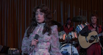 Movie still from “Coal Miner's Daughter” (1980), directed by Michael Apted – A woman dressed as a woman holding a microphone; Medium shot, Over the shoulder angle