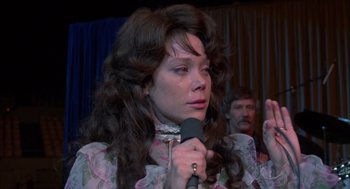 Movie still from “Coal Miner's Daughter” (1980), directed by Michael Apted – A woman with long brown curly hair holding a microphone; Close Up shot, Over the shoulder angle
