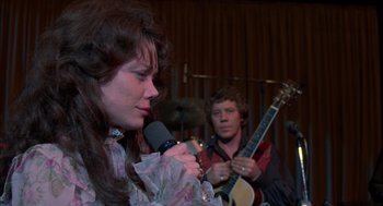 Movie still from “Coal Miner's Daughter” (1980), directed by Michael Apted – A woman holding a microphone while a man plays a guitar; Close Up shot, Over the shoulder angle