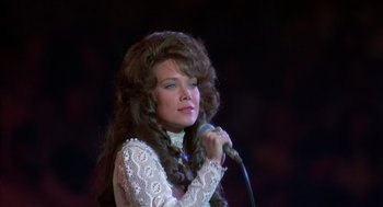 Movie still from “Coal Miner's Daughter” (1980), directed by Michael Apted – A woman in a white dress holding a microphone; Close Up shot, Low angle
