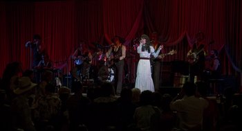 Movie still from “Coal Miner's Daughter” (1980), directed by Michael Apted – A woman in a white dress singing into a microphone on a stage; Wide shot, High angle