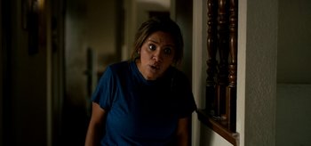 Movie still from “Coast” (2021), directed by Derek Schweickart – A woman standing next to a railing in a room; Medium shot, Over the shoulder angle