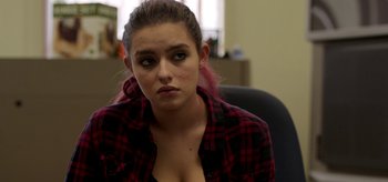 Movie still from “Coast” (2021), directed by Derek Schweickart – A woman sitting in an office chair wearing a red and black plaid shirt; Close Up shot, Over the shoulder angle