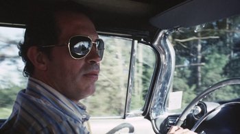 Movie still from “Cockfighter” (1974), directed by Monte Hellman – A man driving a car wearing sunglasses and a striped shirt; Close Up shot, Low angle