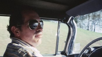 Movie still from “Cockfighter” (1974), directed by Monte Hellman – A man wearing sunglasses sitting in the driver's seat of a car; Close Up shot, Low angle