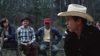 Movie still from “Cockfighter” (1974), directed by Monte Hellman – A group of men sitting on a fence watching another man; Medium shot, Over the shoulder angle