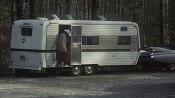 Movie still from “Cockfighter” (1974), directed by Monte Hellman – A man standing in the doorway of a silver trailer; Wide shot, High angle