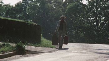 Movie still from “Cockfighter” (1974), directed by Monte Hellman – A man walking down a road with two suitcases; Wide shot, Low angle