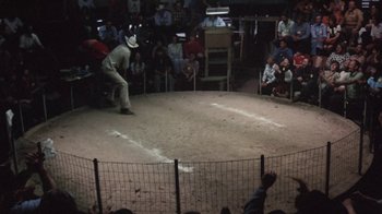 Movie still from “Cockfighter” (1974), directed by Monte Hellman – A man in a cowboy hat is in the middle of an arena; Extreme Wide shot, High angle