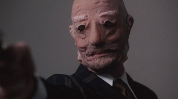 Movie still from “Cockfighter” (1974), directed by Monte Hellman – A man with a bald head wearing a suit and tie; Extreme Close Up shot, Low angle