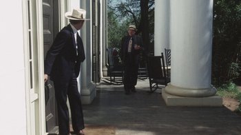 Movie still from “Cockfighter” (1974), directed by Monte Hellman – A man in a suit and a cowboy hat standing on a porch; Wide shot, Over the shoulder angle