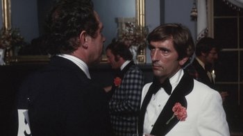 Movie still from “Cockfighter” (1974), directed by Monte Hellman – A man in a suit and tie standing next to another man in a tuxedo; Medium shot, Over the shoulder angle