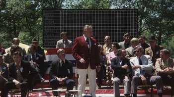 Movie still from “Cockfighter” (1974), directed by Monte Hellman – A man in a red jacket stands in front of a group of people; Wide shot, Over the shoulder angle