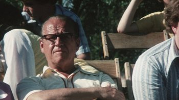 Movie still from “Cockfighter” (1974), directed by Monte Hellman – An older man sitting in a chair with his arms crossed; Close Up shot, Over the shoulder angle