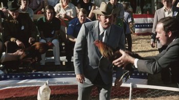 Movie still from “Cockfighter” (1974), directed by Monte Hellman – A man in a suit and hat holding a chicken; Medium shot, Low angle