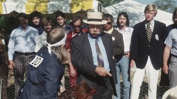 Movie still from “Cockfighter” (1974), directed by Monte Hellman – An old man in a suit and a hat is standing in front of a group of people; Medium shot, Over the shoulder angle