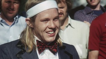 Movie still from “Cockfighter” (1974), directed by Monte Hellman – A man with long blonde hair wearing a bow tie; Close Up shot, Over the shoulder angle