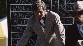 Movie still from “Cockfighter” (1974), directed by Monte Hellman – A man wearing a suit and tie standing in front of a chalkboard; Medium shot, Low angle
