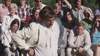 Movie still from “Cockfighter” (1974), directed by Monte Hellman – A group of people sitting and standing around a man in a white shirt; Medium shot, Over the shoulder angle