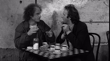 Movie still from “Coffee and Cigarettes” (2003), directed by Jim Jarmusch – Two men sitting at a table with cups of coffee; Medium shot, Over the shoulder angle