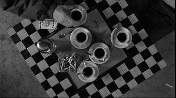 Movie still from “Coffee and Cigarettes” (2003), directed by Jim Jarmusch – Four cups of coffee on a checkerboard table; Wide shot, Overhead angle