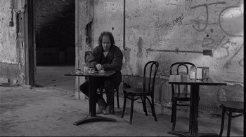 Movie still from “Coffee and Cigarettes” (2003), directed by Jim Jarmusch – A man sitting at a table in front of two chairs; Wide shot, High angle