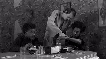 Movie still from “Coffee and Cigarettes” (2003), directed by Jim Jarmusch – Three people sitting at a table and one is pouring something in a cup; Medium shot, Low angle