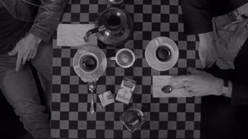 Movie still from “Coffee and Cigarettes” (2003), directed by Jim Jarmusch – A black and white photo of a table with cups and a tea pot on it; Wide shot, Overhead angle