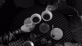 Movie still from “Coffee and Cigarettes” (2003), directed by Jim Jarmusch – A black and white photo of two people holding cups of coffee; Medium shot, Overhead angle