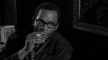 Movie still from “Coffee and Cigarettes” (2003), directed by Jim Jarmusch – A black and white photo of a man eating a piece of food; Close Up shot, Over the shoulder angle