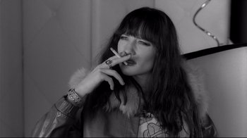 Movie still from “Coffee and Cigarettes” (2003), directed by Jim Jarmusch – A woman smoking a cigarette while wearing a jacket; Close Up shot, High angle