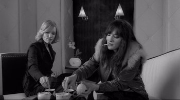 Movie still from “Coffee and Cigarettes” (2003), directed by Jim Jarmusch – Two women sitting at a table and one of the women is smoking a cigarette; Medium shot, High angle
