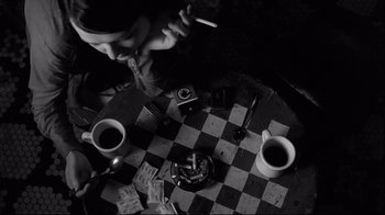 Movie still from “Coffee and Cigarettes” (2003), directed by Jim Jarmusch – A person sitting at a table with coffee and cigarettes; Medium shot, Overhead angle