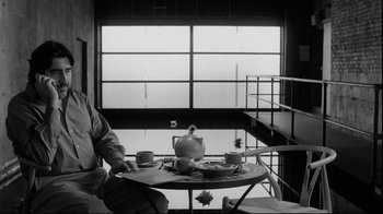 Movie still from “Coffee and Cigarettes” (2003), directed by Jim Jarmusch – A person sitting at a table with a tea pot and cups; Medium shot, High angle