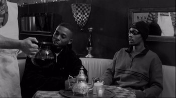 Movie still from “Coffee and Cigarettes” (2003), directed by Jim Jarmusch – Two young men sitting at a table in front of a tea pot; Medium shot, High angle