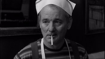 Movie still from “Coffee and Cigarettes” (2003), directed by Jim Jarmusch – An older man wearing an apron and holding a cigarette in his mouth; Close Up shot, Low angle