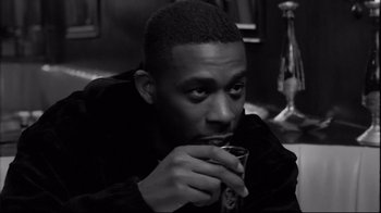 Movie still from “Coffee and Cigarettes” (2003), directed by Jim Jarmusch – A black and white photo of a man drinking a cup of coffee; Close Up shot, Over the shoulder angle