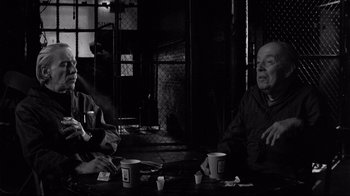 Movie still from “Coffee and Cigarettes” (2003), directed by Jim Jarmusch – Two people sitting at a table with cups; Medium shot, Over the shoulder angle