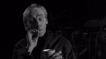 Movie still from “Coffee and Cigarettes” (2003), directed by Jim Jarmusch – A man smoking a cigarette while holding a cup of coffee; Medium shot, Low angle