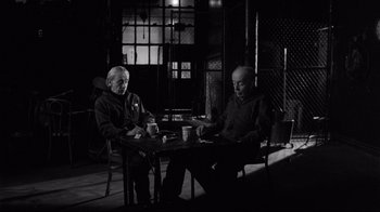Movie still from “Coffee and Cigarettes” (2003), directed by Jim Jarmusch – A man and a woman sitting at a table with cups; Medium shot, High angle