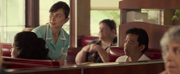 Movie still from “Cold in July” (2014), directed by Jim Mickle – A woman sitting at a table in front of two other people; Medium shot, Over the shoulder angle