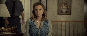 Movie still from “Cold in July” (2014), directed by Jim Mickle – A woman in a blue vest standing in front of a wall; Close Up shot, Over the shoulder angle