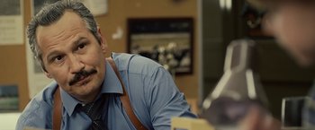 Movie still from “Cold in July” (2014), directed by Jim Mickle – A person sitting at a table; Close Up shot, Over the shoulder angle