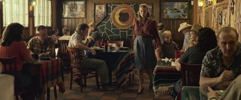 Movie still from “Cold in July” (2014), directed by Jim Mickle – A woman standing in front of a man and two children in a room; Medium shot, Over the shoulder angle