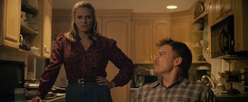 Movie still from “Cold in July” (2014), directed by Jim Mickle – A woman standing next to a man sitting in a kitchen; Medium shot, Over the shoulder angle